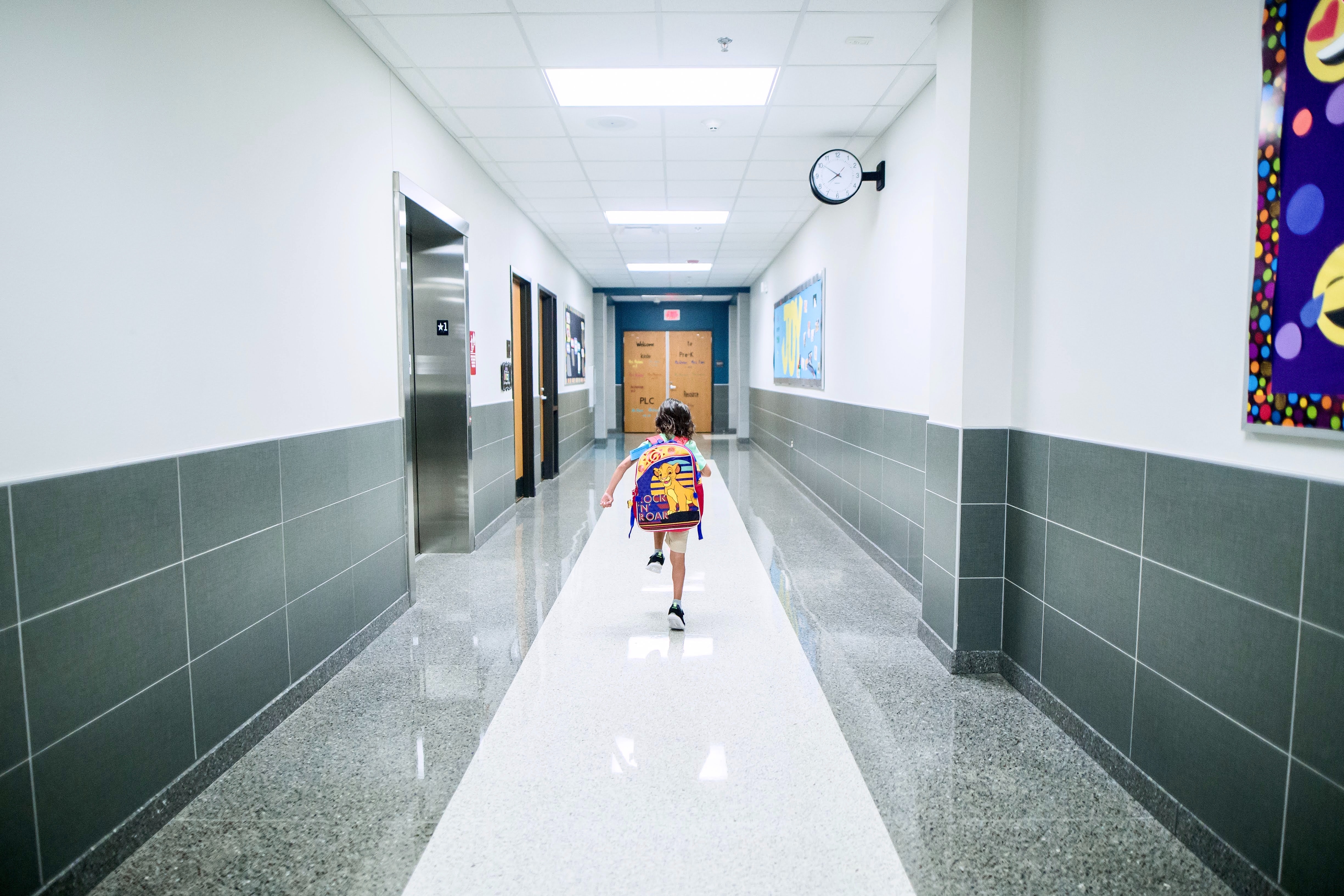 Child with backpack walking down a hallway at a school.