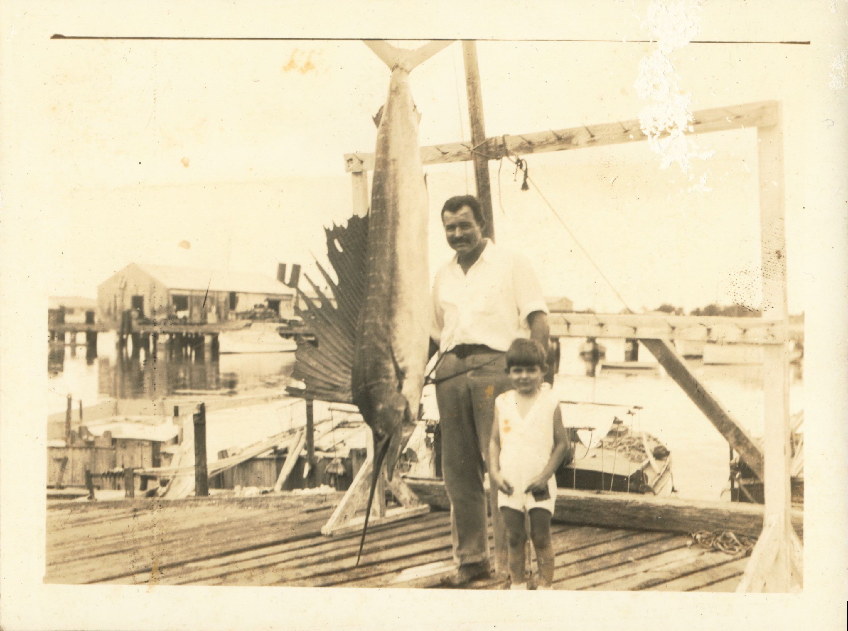 white father and young son standing on dock by large hanging fish