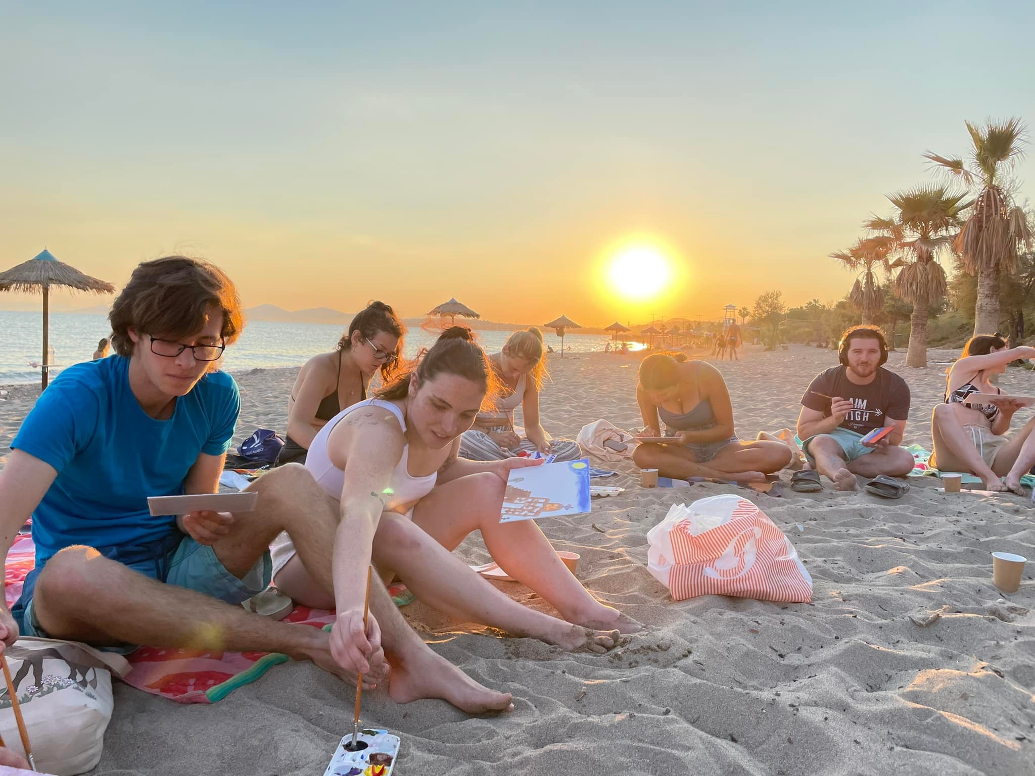 The students spontaneously organized a collaborative painting activity on the beach at sunset.