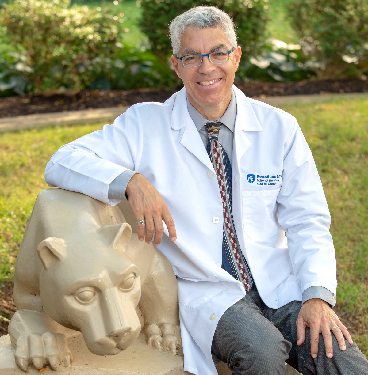 Dr. David Rabago sits near a statue of the nittany lion on Penn State College of Medicine's campus. 