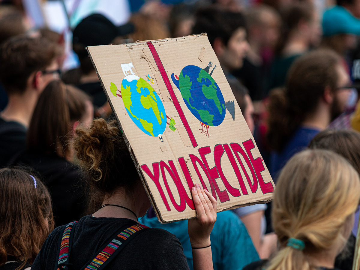 A group of young protesters with a cardboard sign showing two Earths and the words "You Decide"