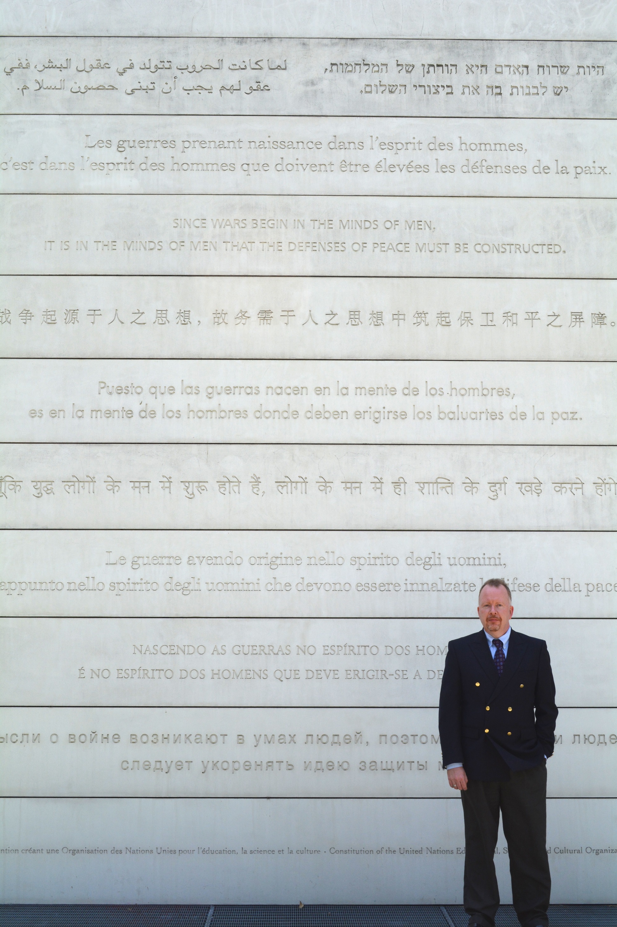 A man in front of the UNESCO Peace Wall with writing in various languages