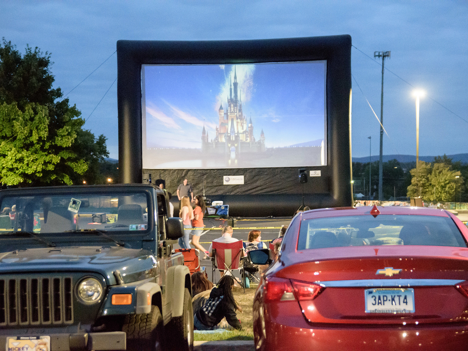 Inflatable rmovie screen with Disney insignia on it and cars parked in a lot in front of it.