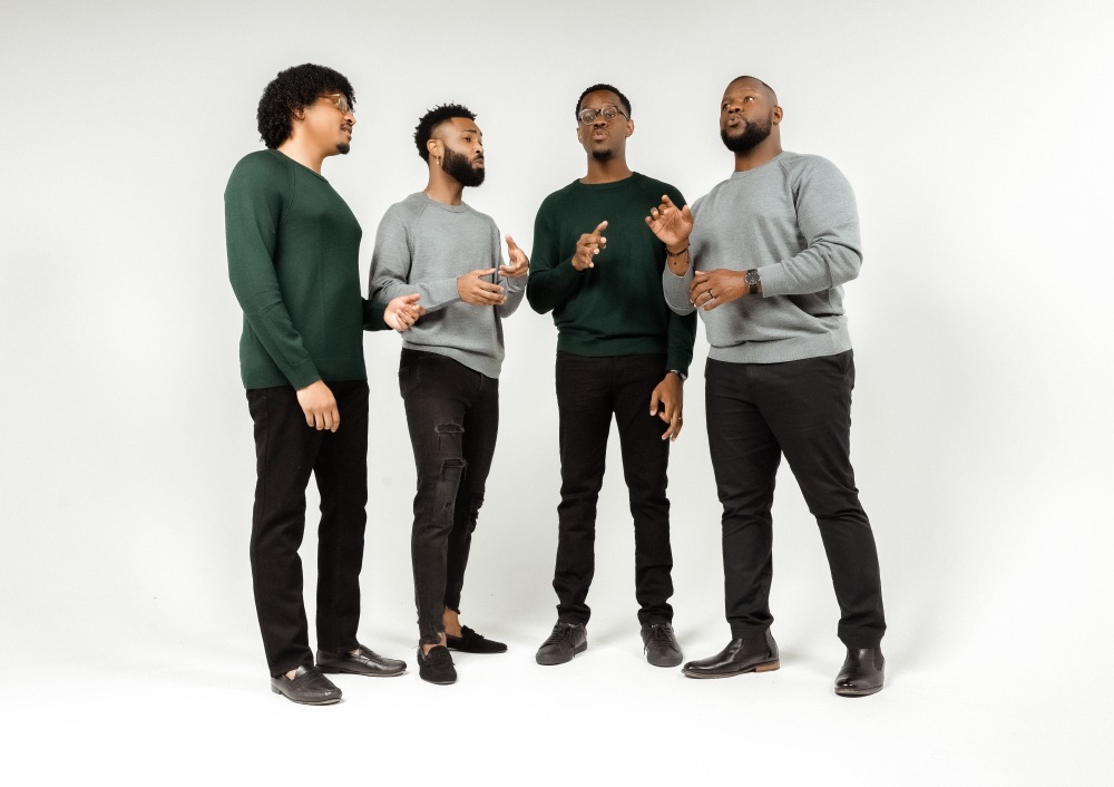 Four men of color stand in a semi-circle and sing in unison.