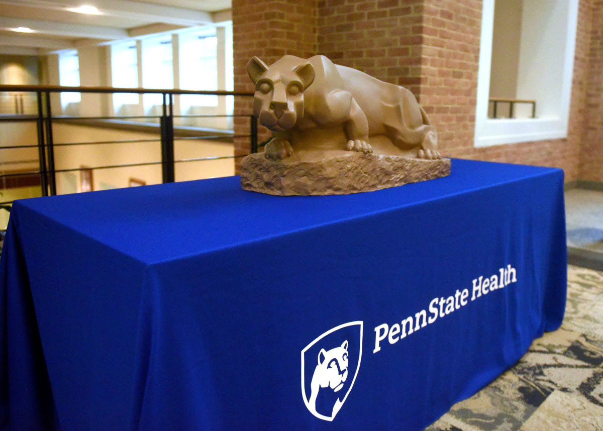 A lion statue sits on a table. The table is covered with a blue cloth that says, "Penn State Health."