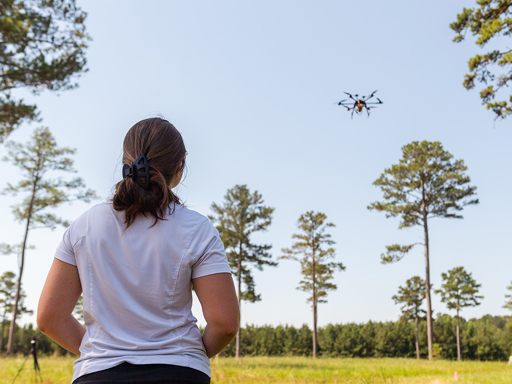 An individual operates a drone in a forested area. 