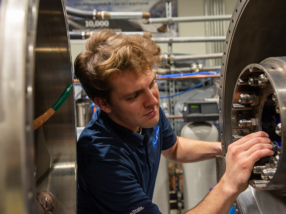 A person adjusts a bolt in a large silver cavity. 