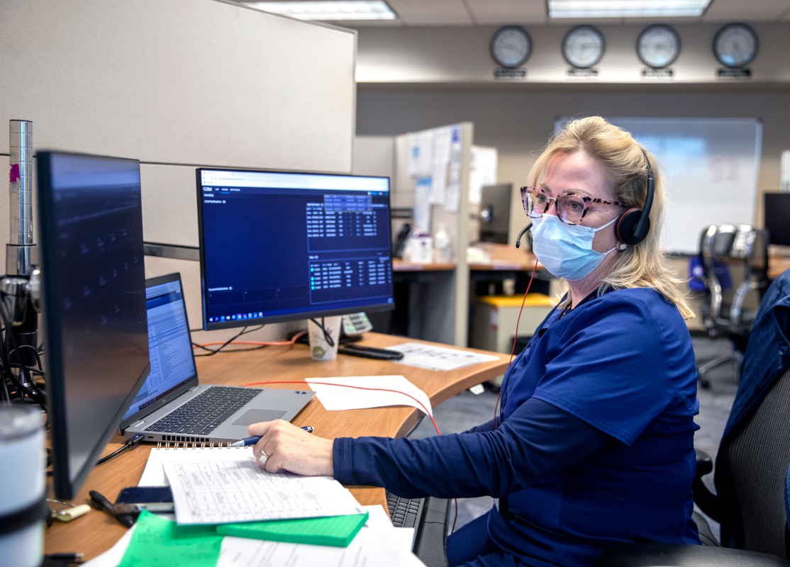 A nurse wearing scrubs sits at a computer doing a virtual visit with a patient