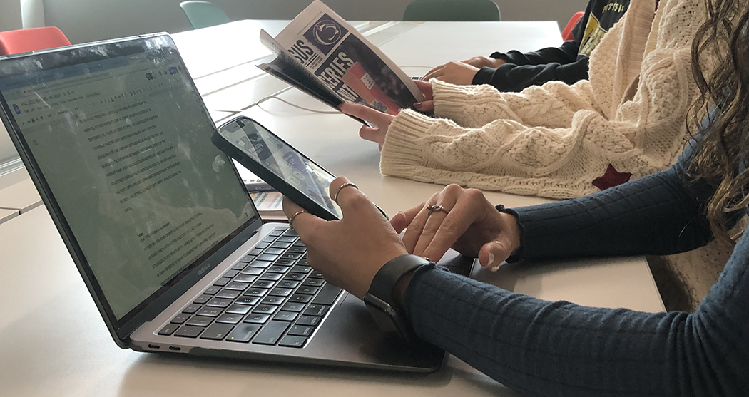 Students at laptop, with smartphone and newspaper