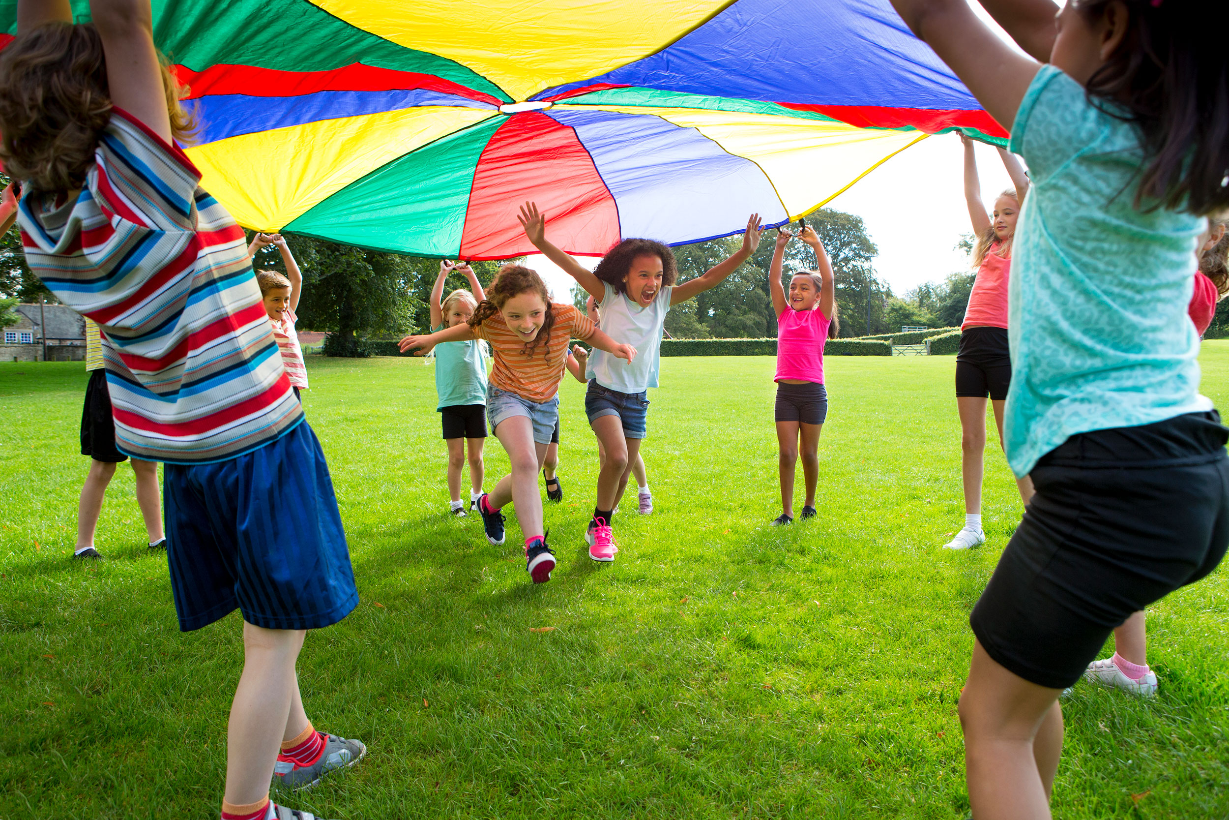 children playing in a field under a colorful parachute