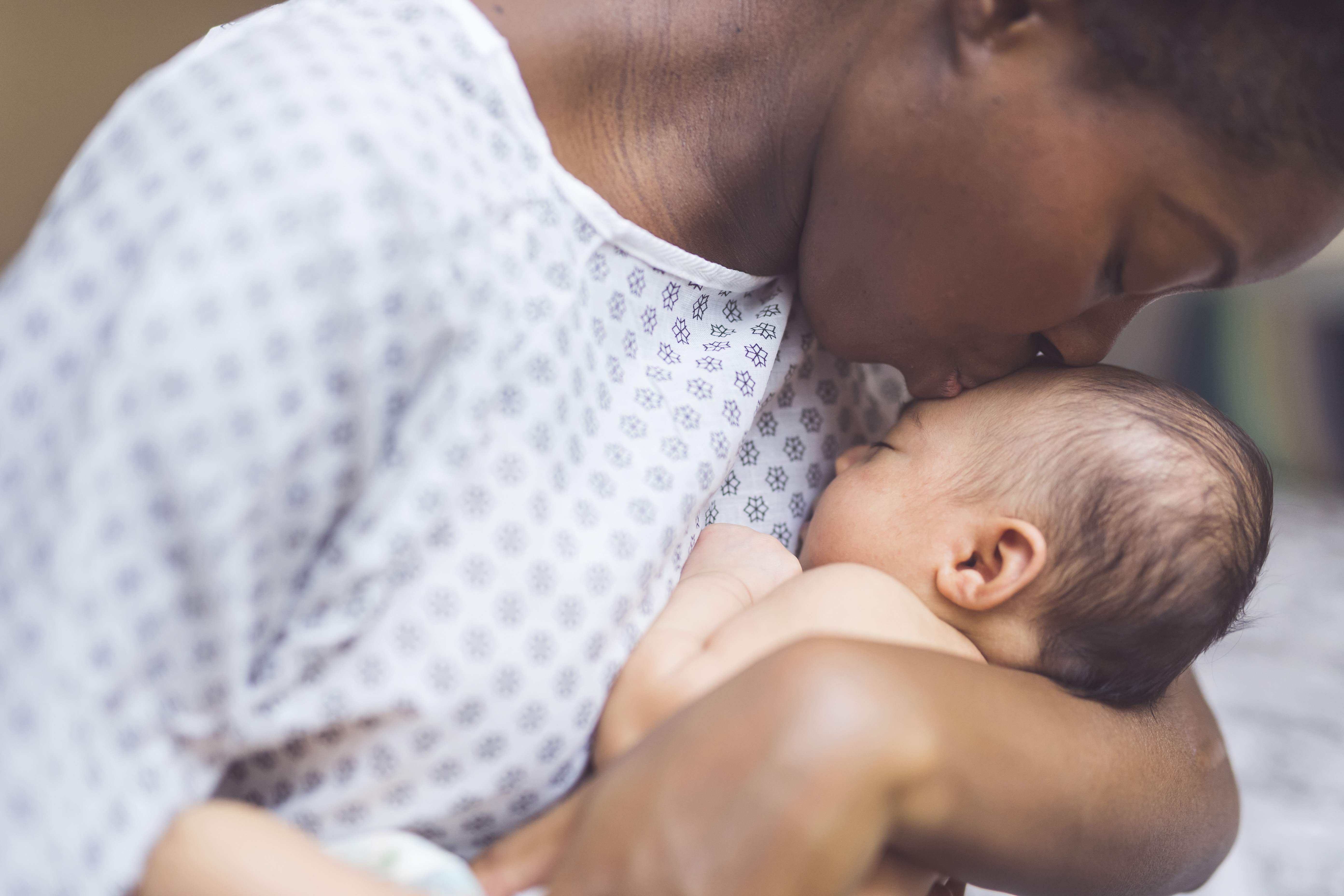 Mother wearing hospital gown kisses newborn gently on the head