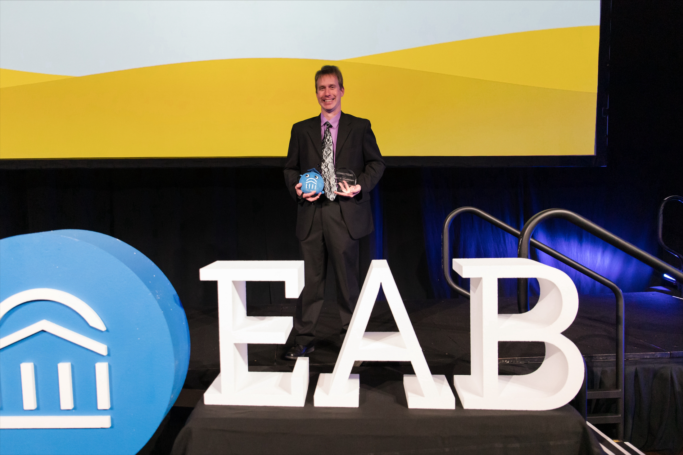 John Ellenberger posing on stage holding awards