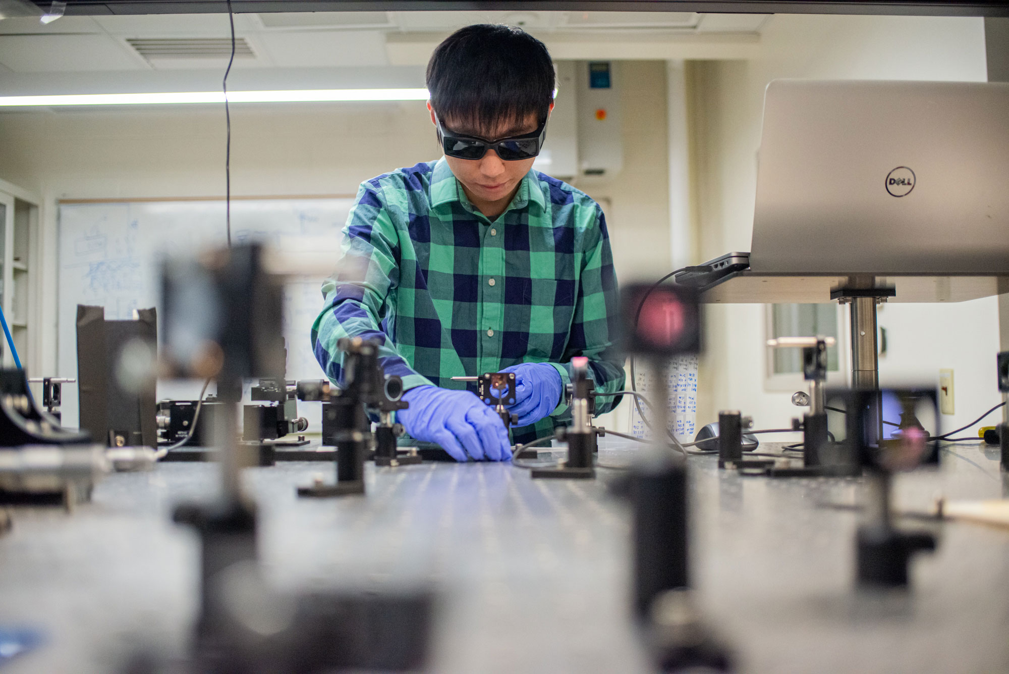 Kyle Lynn, wearing gloves and goggles, works in the lab