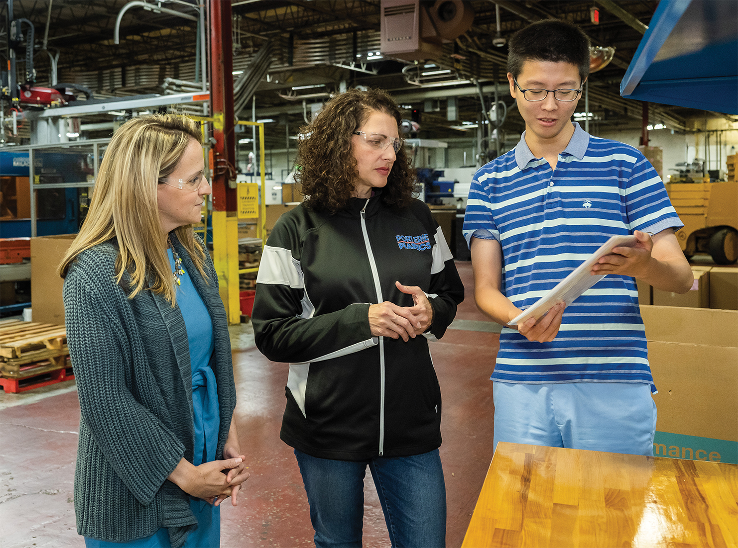 A Penn State Behrend student shows a sign he translated to a professor and a corporate executive during a visit to the shop floor at Port Erie Plastics.