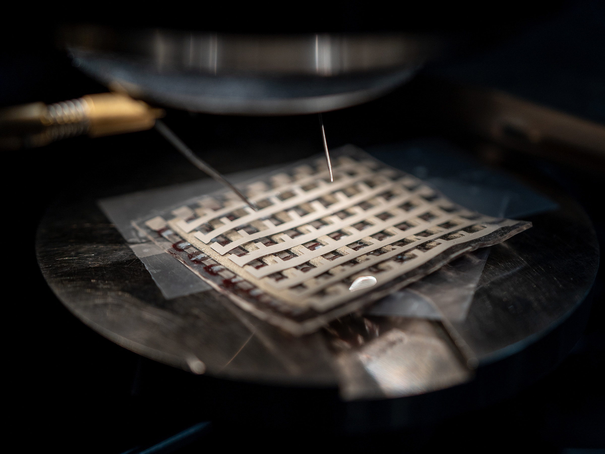 A small metallic device with a metal pattern resembling a basket weave is seen under a light. 