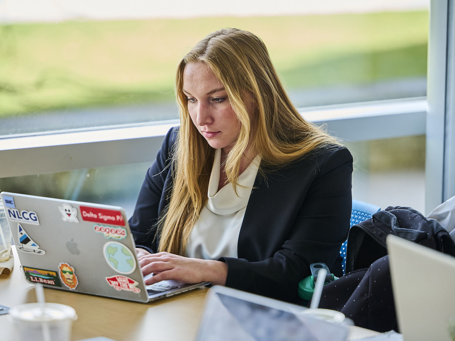 A young woman sits at a table typing on a laptop.