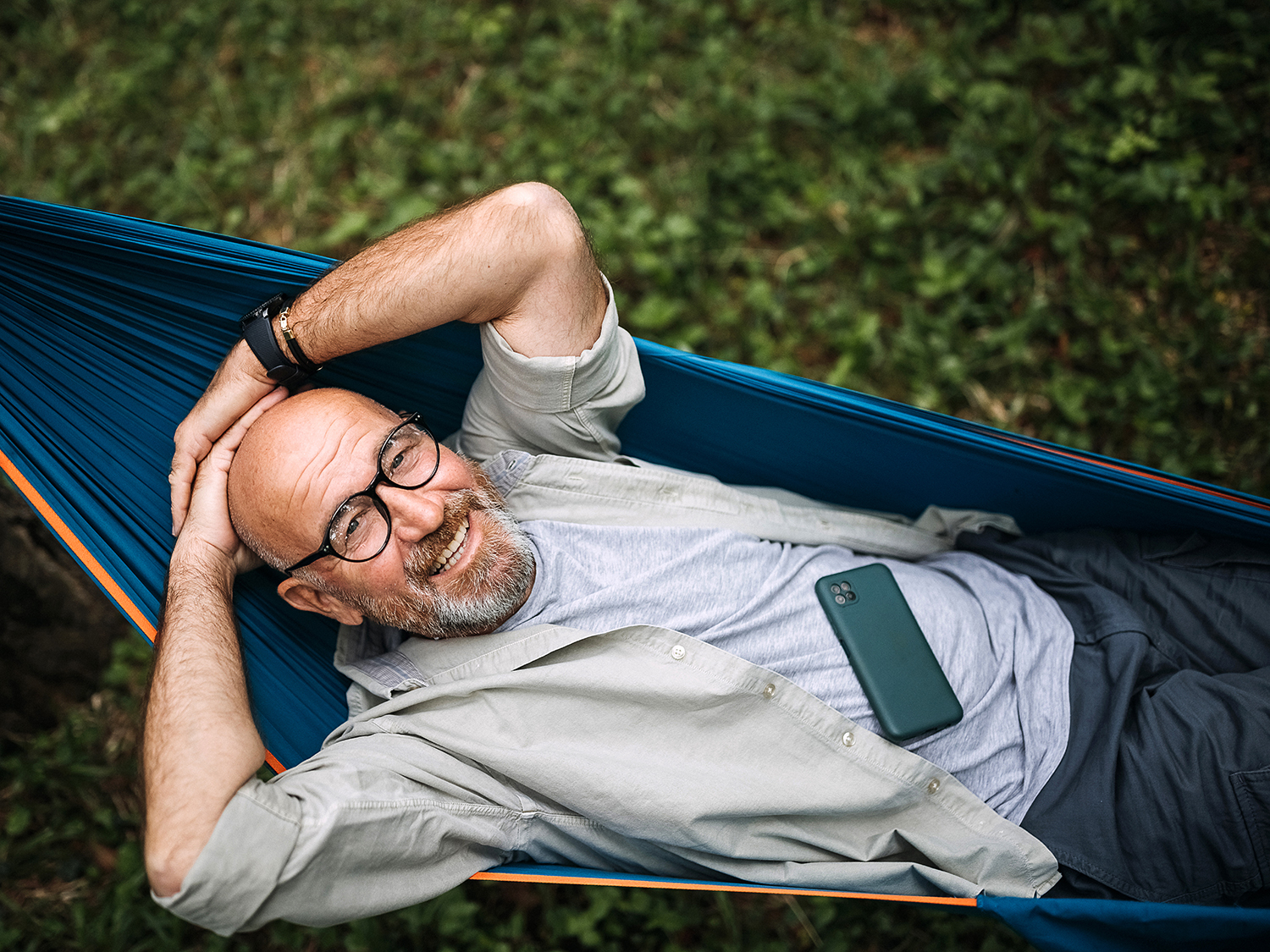 Senior man laying on hammock in nature and using smart phone