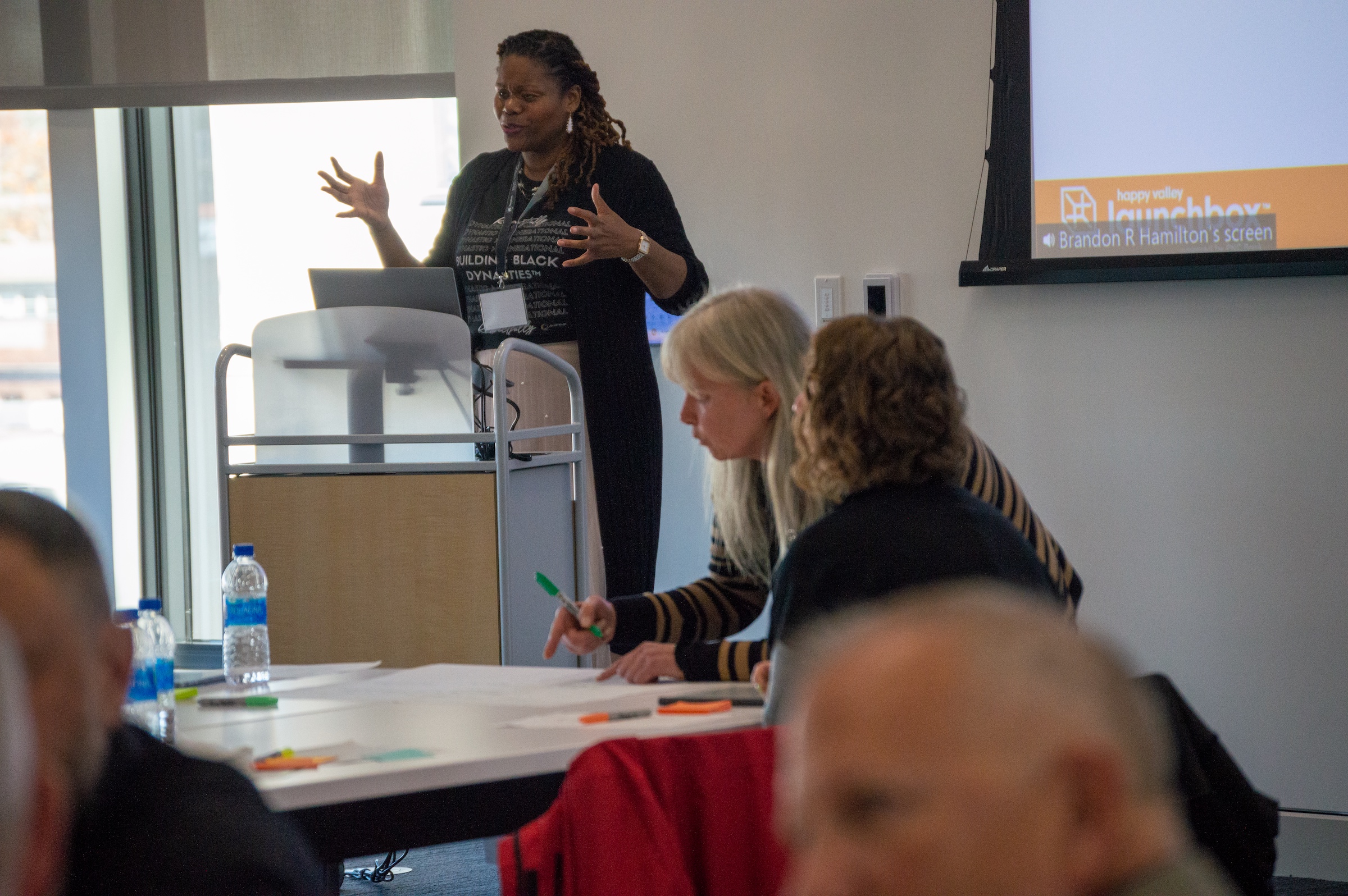 Woman at podium leads exercise with conference attendees at table