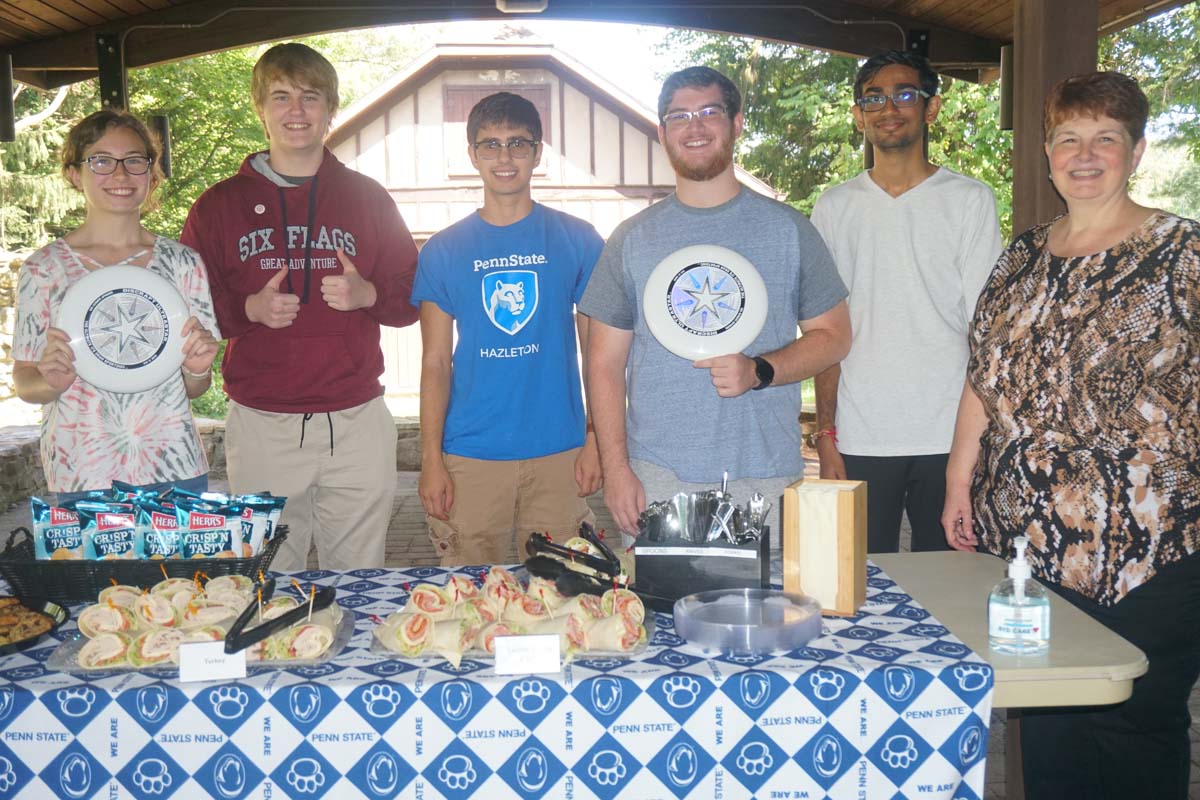 Students holding frisbees under an outdoor pavillion.