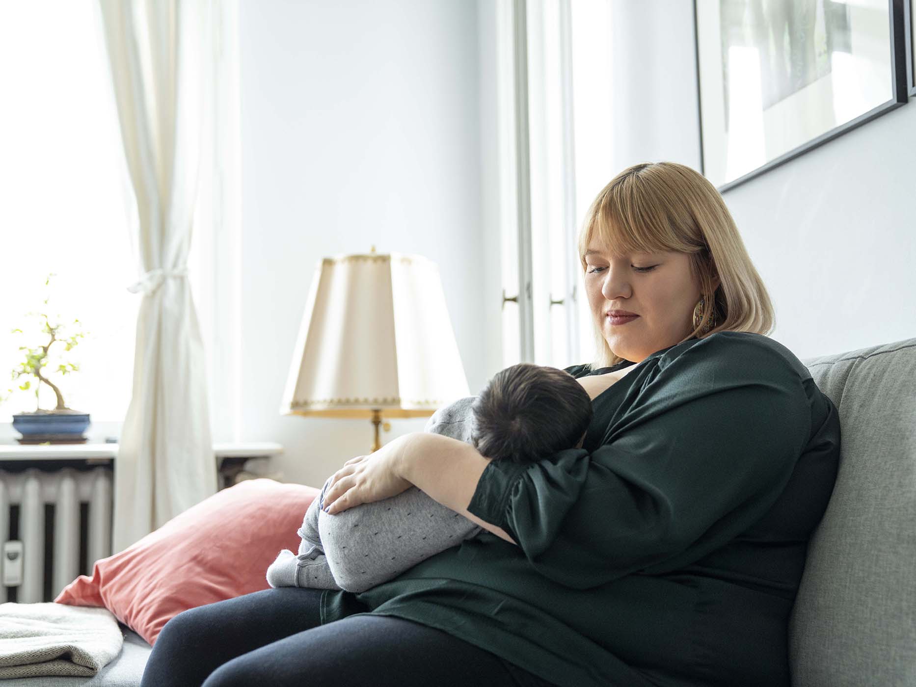 Woman sits on a couch breastfeeding a baby