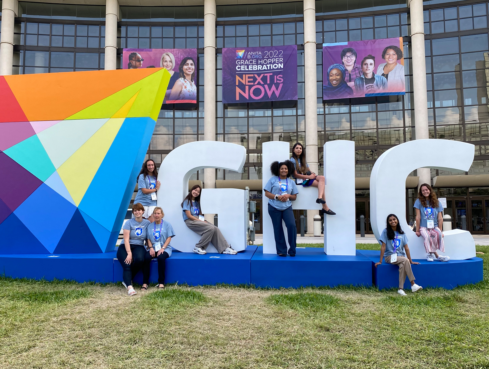 At the Grace Hopper Celebration, eight women sit and stand on giant letters reading GHC. 