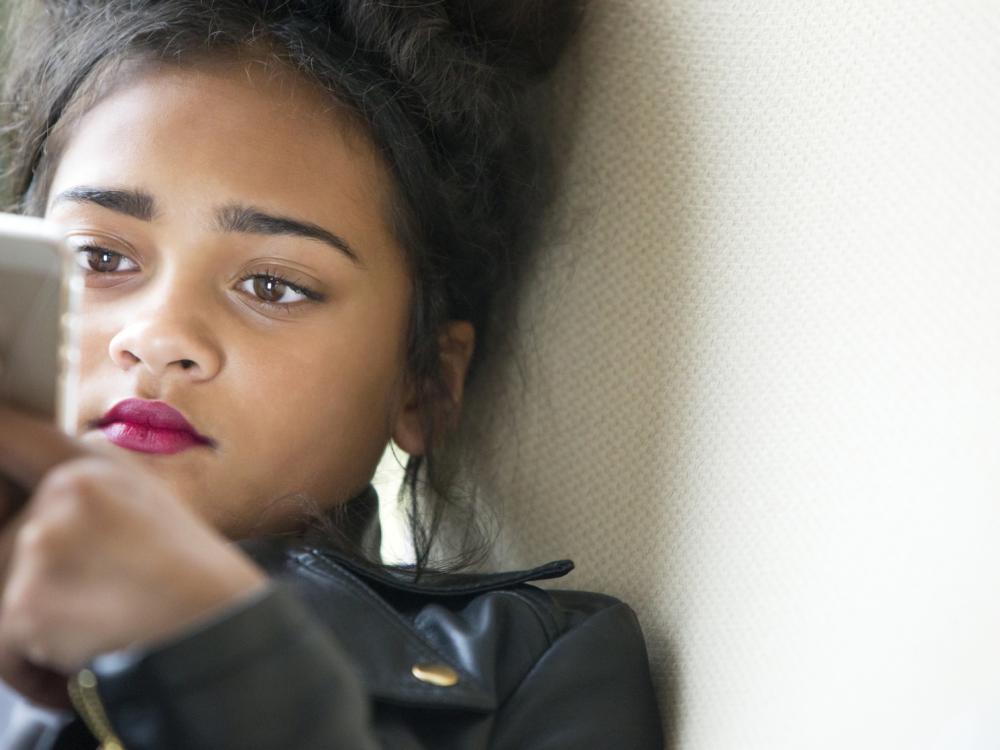 Teenage girl in black jacket looks at her phone