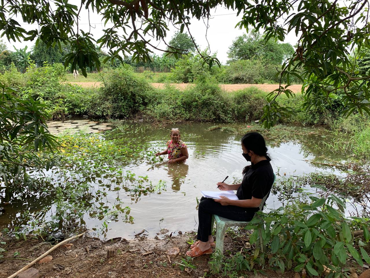 A researcher sits on the bank of a river talking to a woman standing in the water