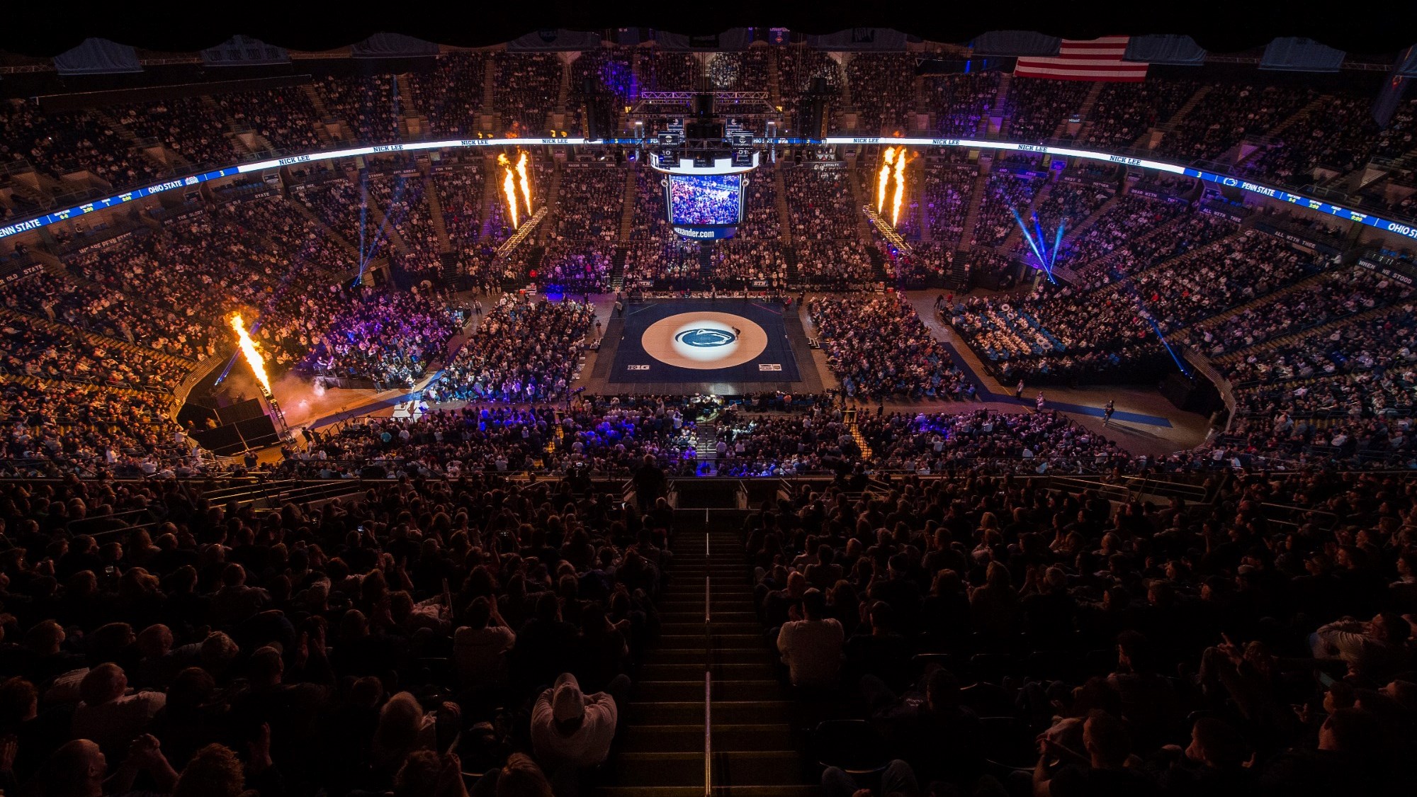 The interior of the Bryce Jordan Center with a packed crowd looking on at a wrestling mat in the center of the arena