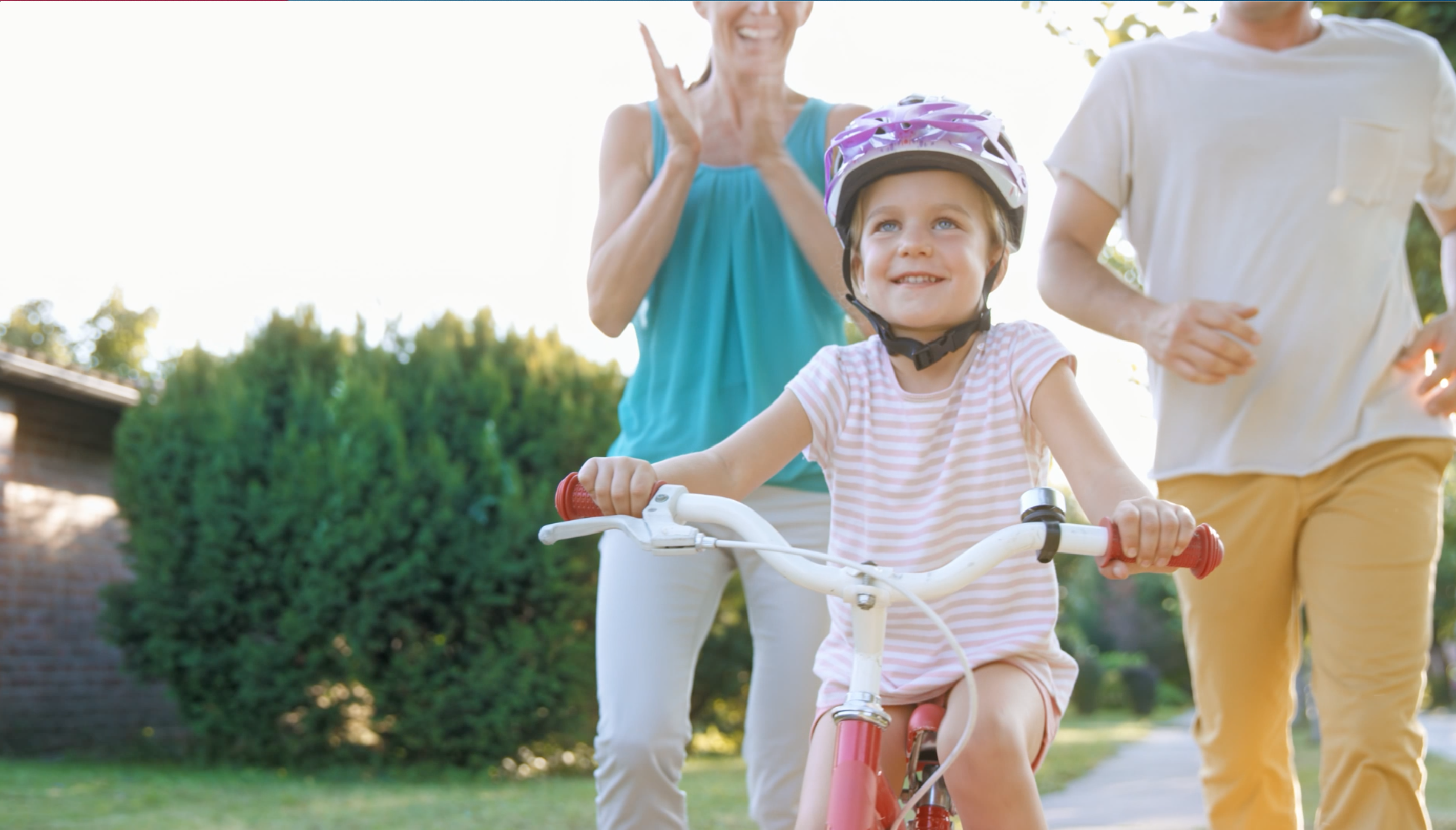 Happy child rides bike while parents watch in the background