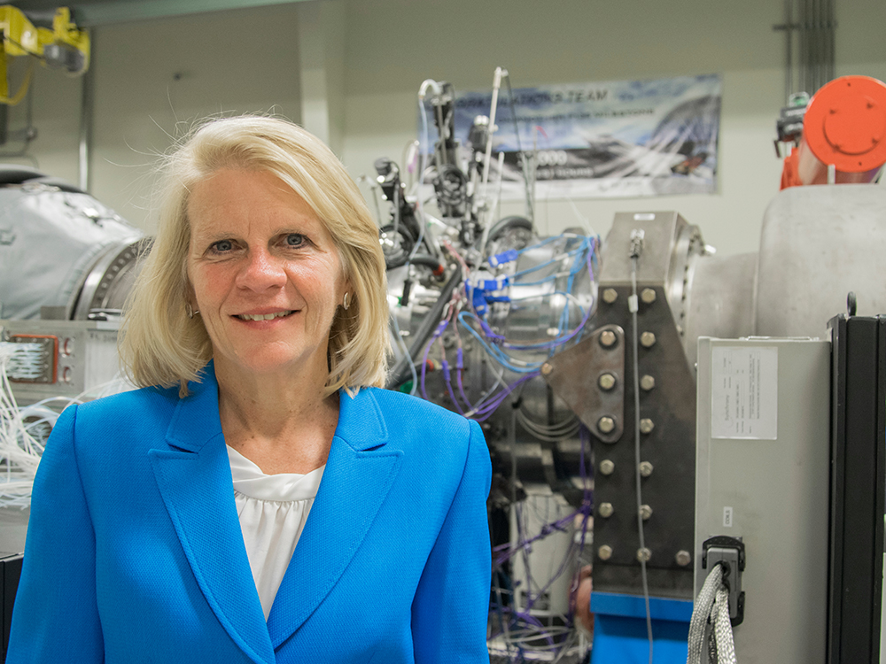 Blonde-haired woman in business attire poses in front of turbine equipment.