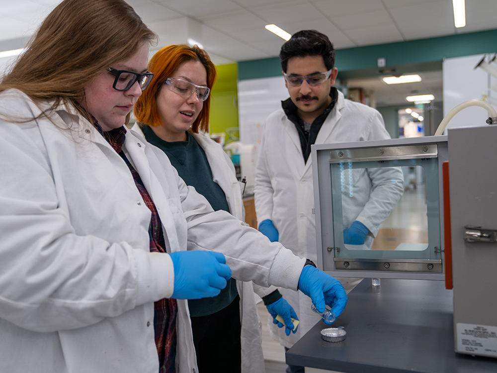 Three scientists in lab coats and blue gloves manipulate a sample of hairy cellulose nanocrystals.