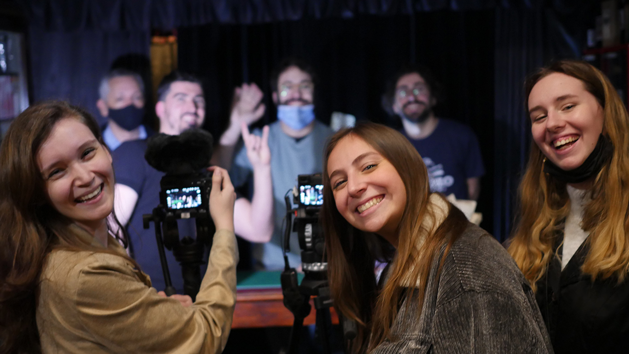 Three smiling students in the foreground with the subject of their focus behind them