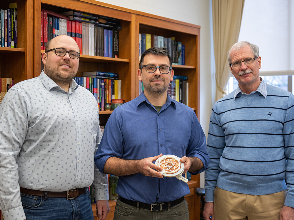 Three individuals pose in an office displaying a small antenna device.