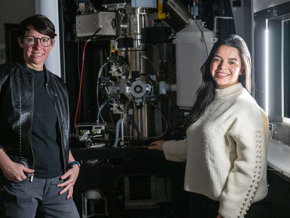 Two individuals stand next to a cryo-electron microscopy machine in a lab.