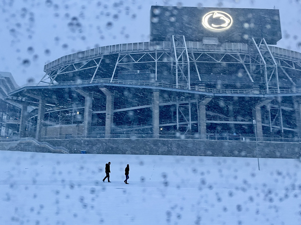 Two individuals walk past Beaver Stadium on a snowy winter day