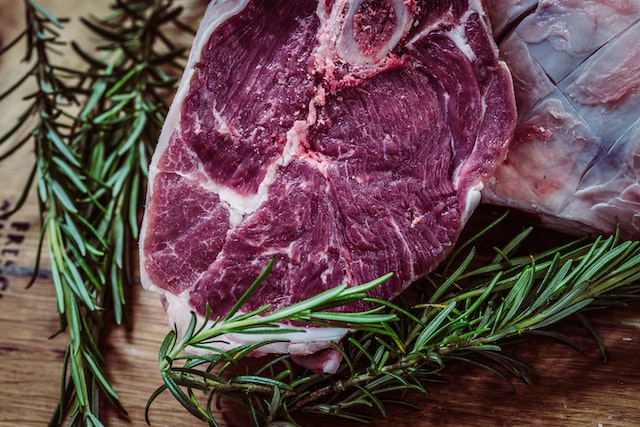 Raw steak resting on a cutting board next to sprigs of rosemary