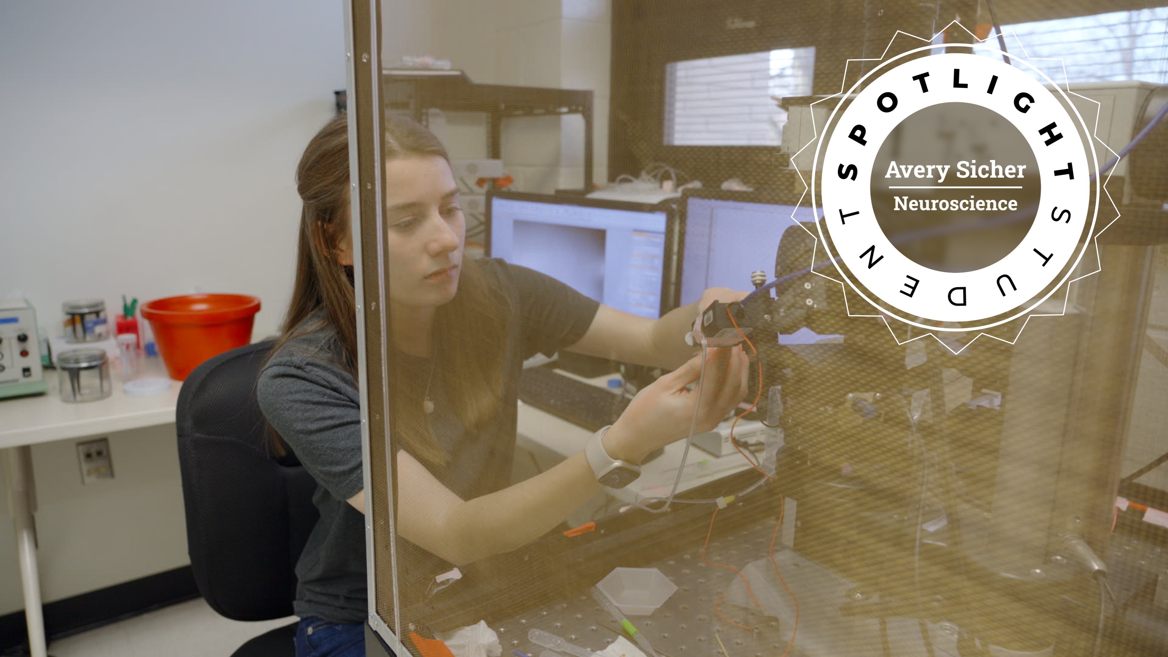 Avery Sicher seated at a lab bench, working with a scientific instrument