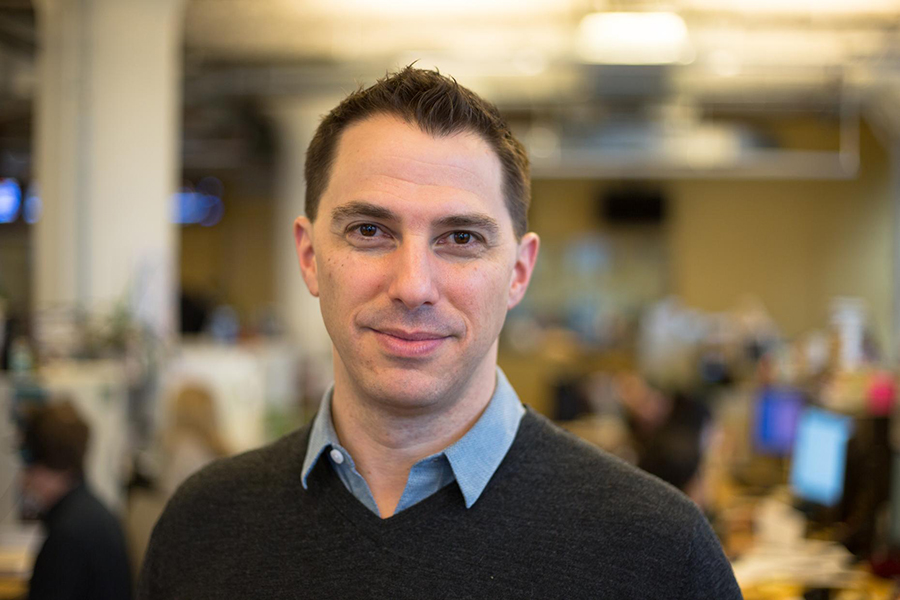 Portrait of Todd Zwillich, smiling, dark haired with collard shirt and sweater