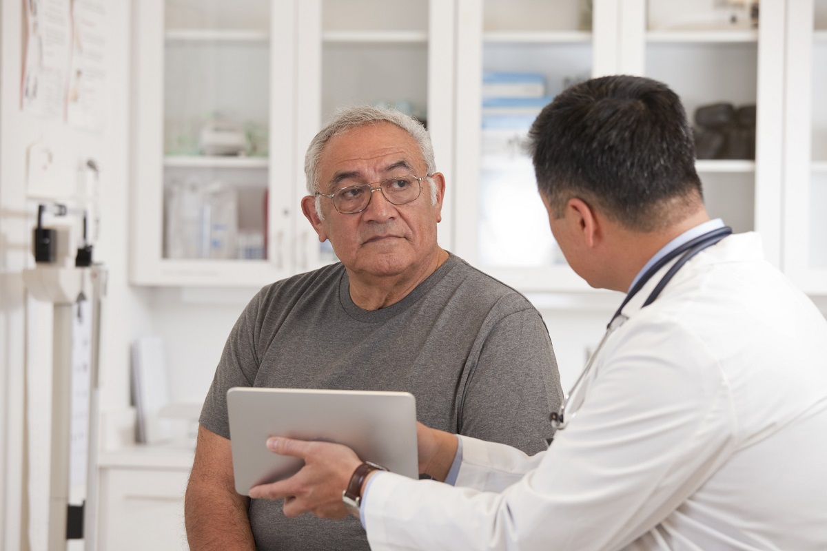 A doctor holds a digital tablet as he talks with a man.