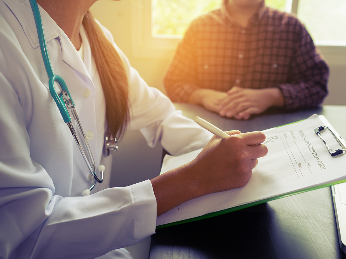 A health care worker takes notes while interviewing a patient