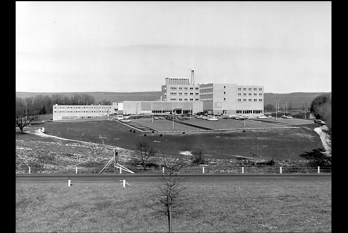 A black-and-white image of a hospital image with rolling hills in the background.