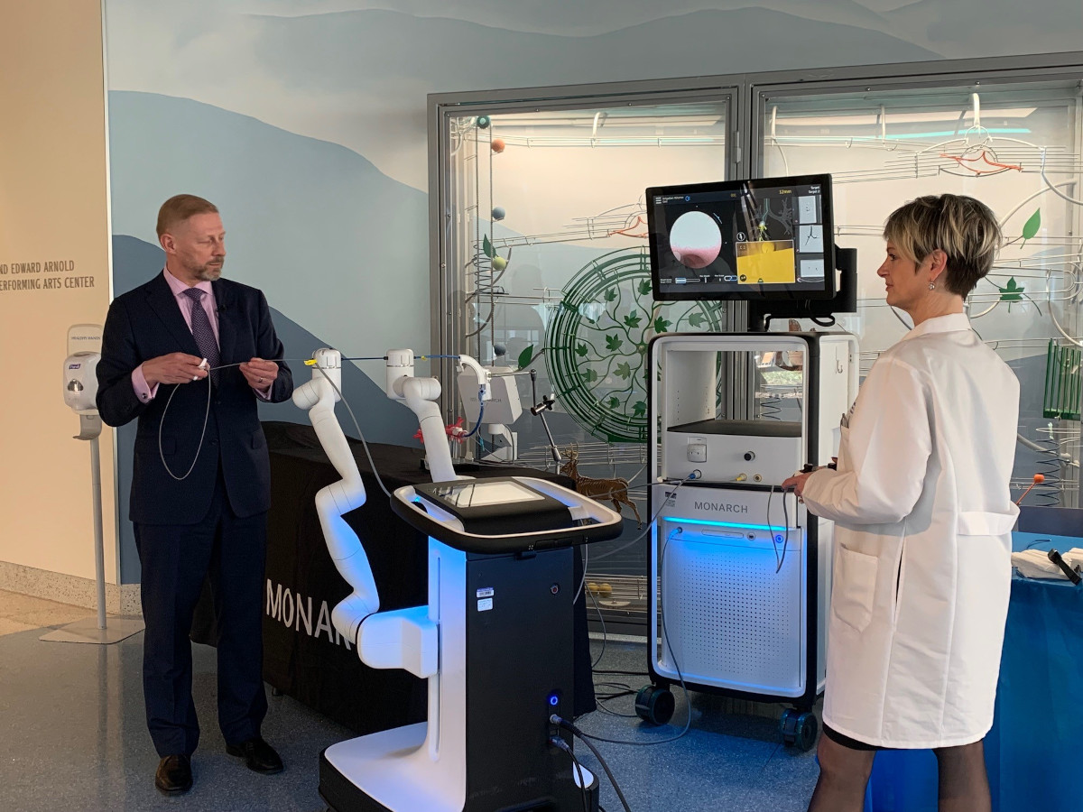 A man and a woman stand next to a robotic bronchoscopy too to demonstrate how it works.