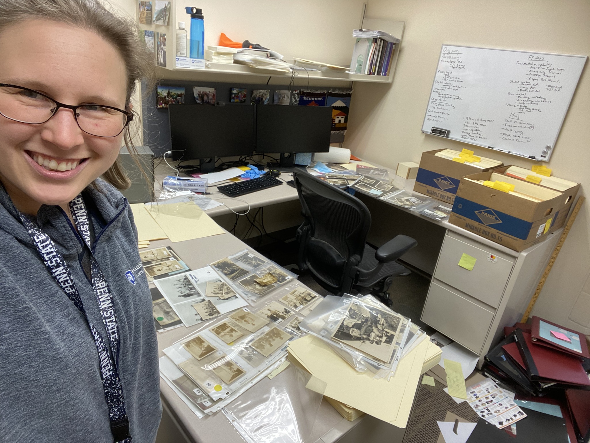 woman by desk with organized piles of old photographs and boxes of files