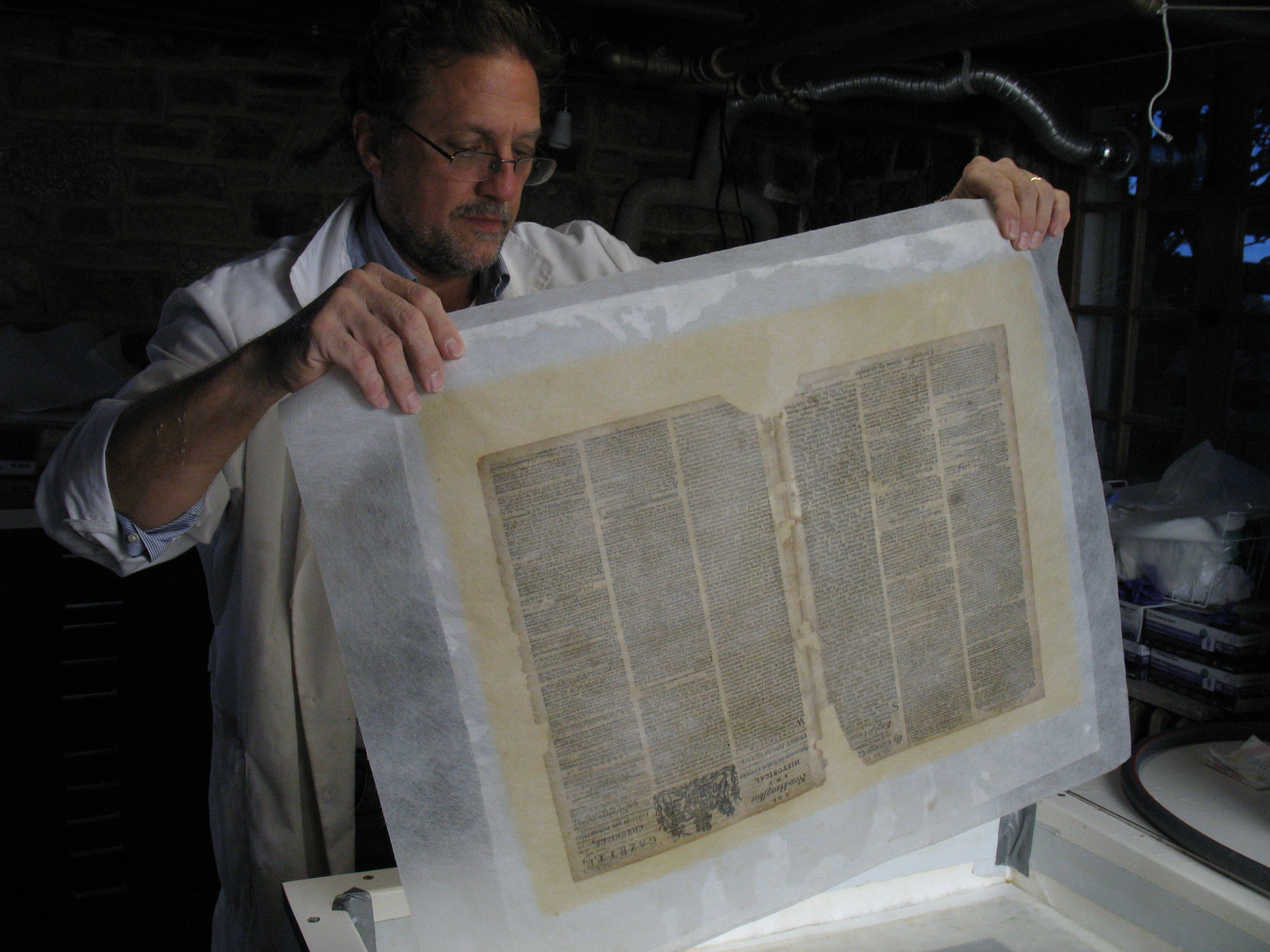 man holding large sheets of sheer paper encasing two pages of old printed newspaper