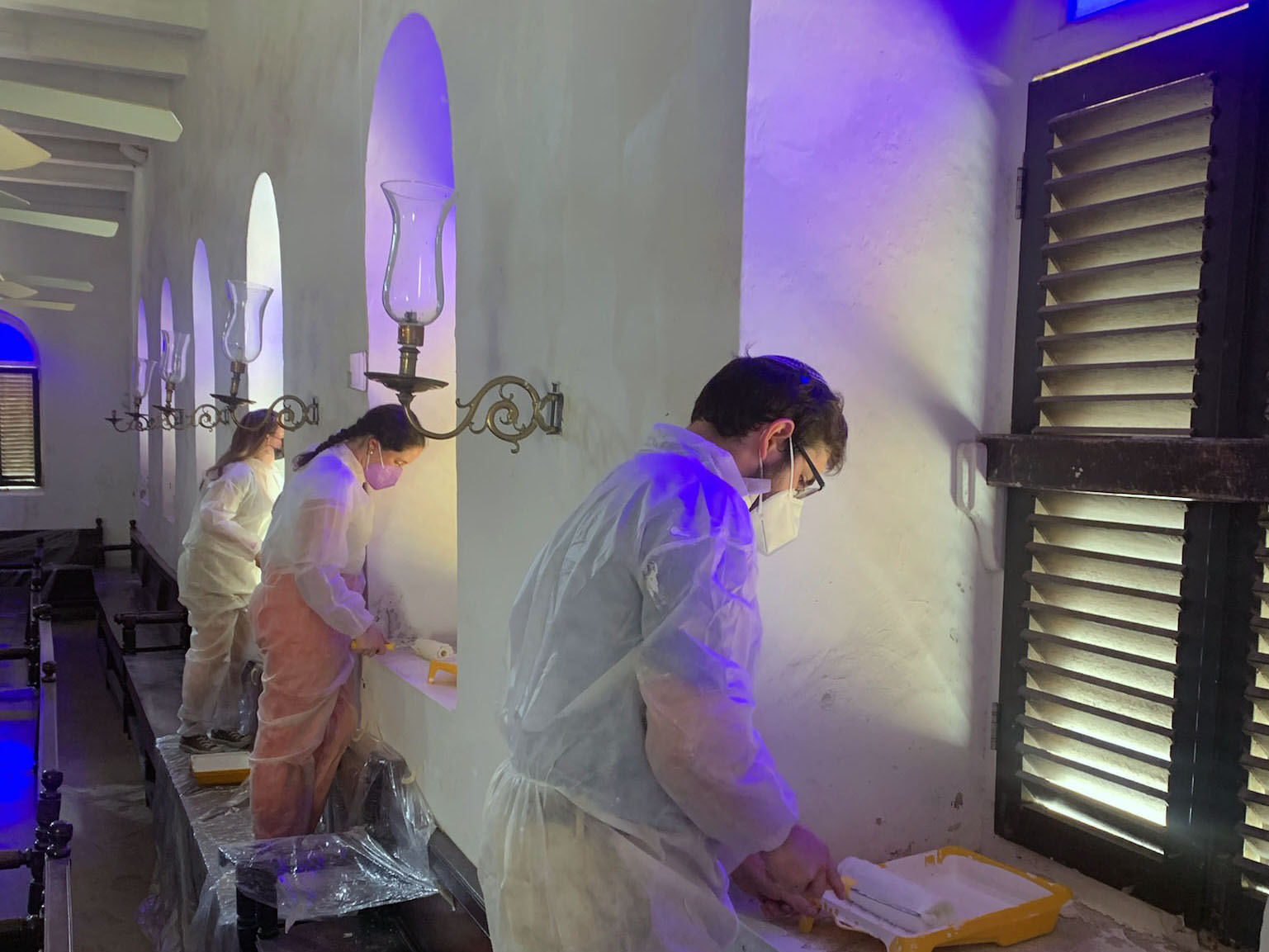 Three students work to restore and repaint windows inside a synagogue,