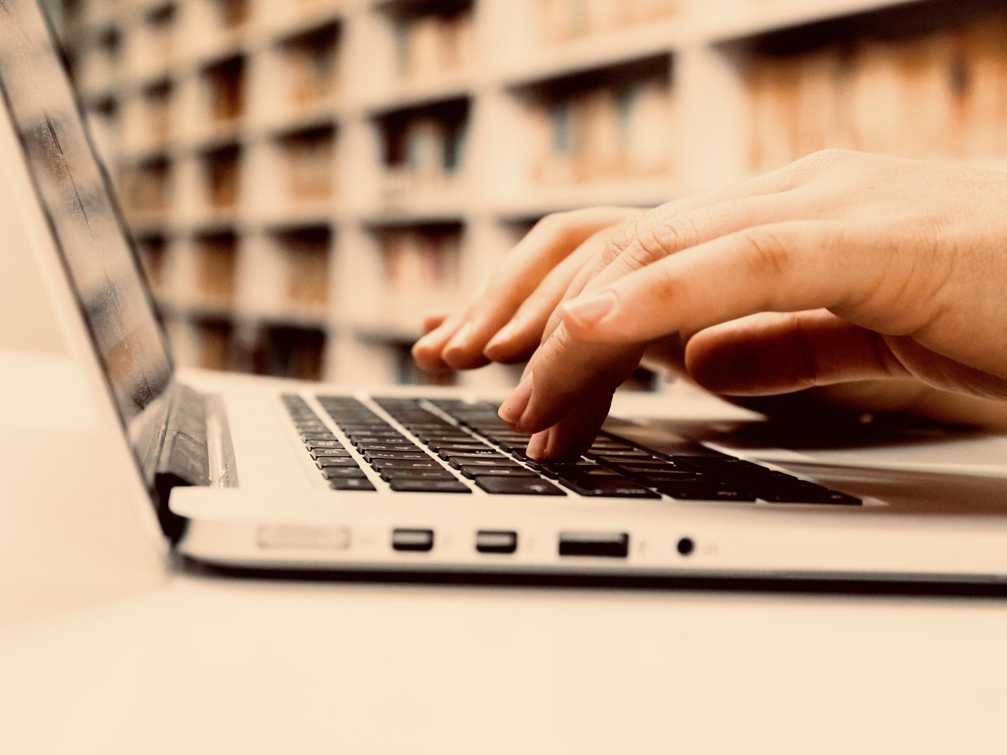 person typing on laptop near library bookshelves