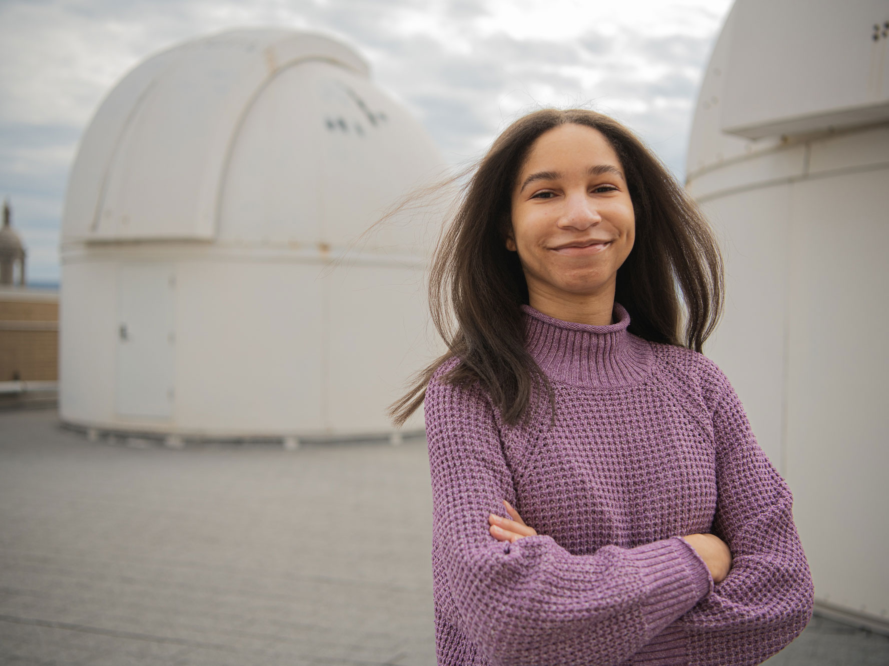 Williams smiles and crosses arms in front of rooftop observatory