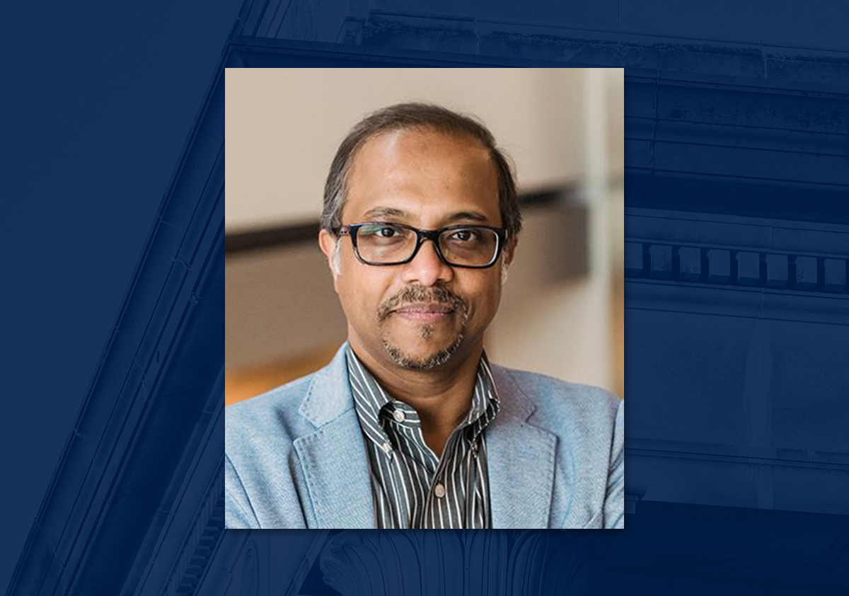 Man with glasses and goatee and wearing light- blue jacket and striped shirt poses with arms crossed for portrait. 