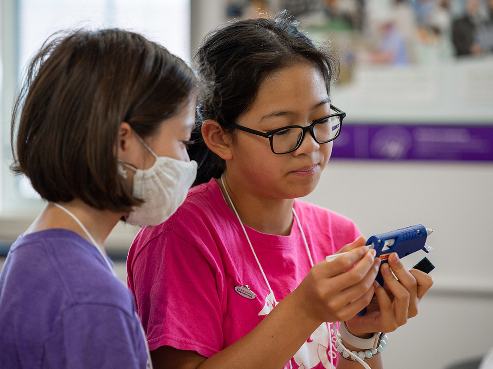 Two students stand together preparing a hot glue gun for use.