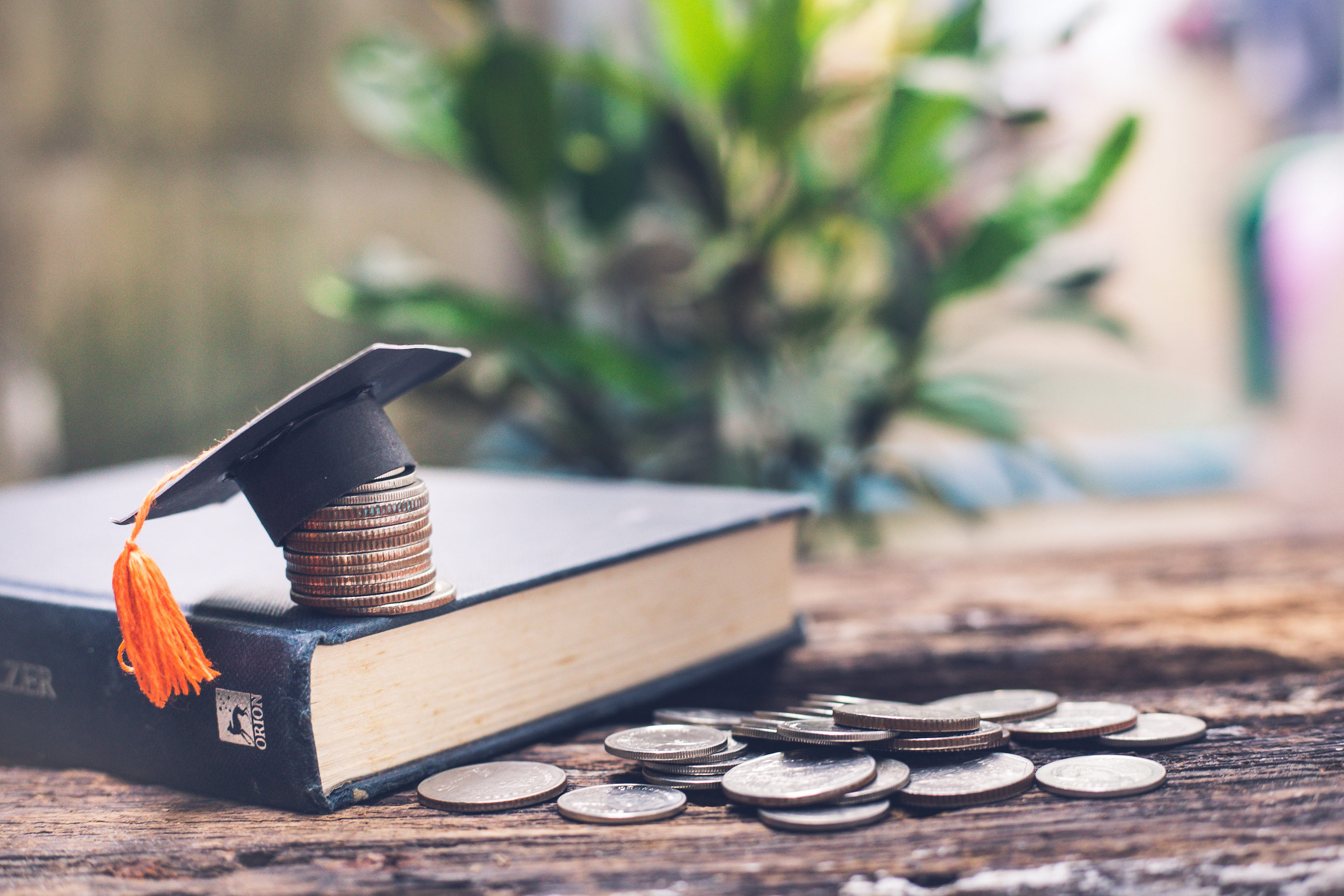 coin pile near book, coin stack on book cover and paper graduation cap atop stack